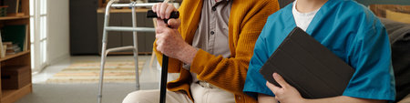 Senior Caucasian man sitting with walking cane next to young adult Latin woman in medical scrubs...