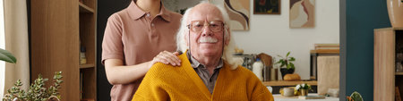 Senior Caucasian man sitting in wheelchair smiling at camera with young adult woman, standing behind...