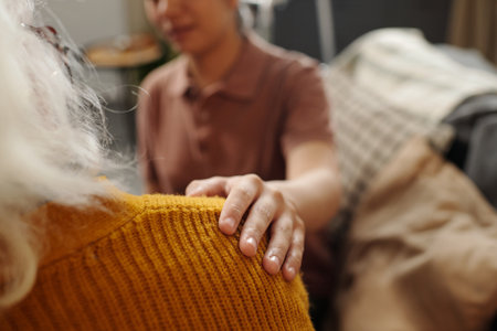 Young adult Asian woman comforting senior Caucasian woman by gently placing hand on shoulder,...