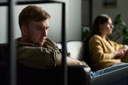 Caucasian young adult man sitting on sofa looking away with serious expression, Caucasian young...
