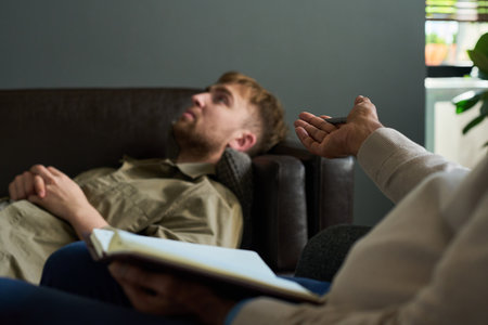 Caucasian young adult man reclining on sofa during therapy session, listening to middle aged...
