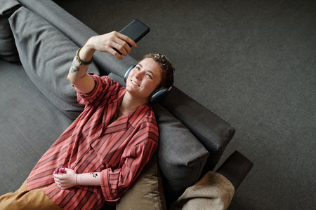 Caucasian young adult woman with prosthetic arm while holding smartphone above head wearing...