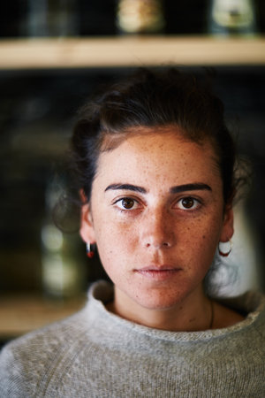 Portrait of young adult Caucasian woman looking directly at camera with neutral expression, dark...