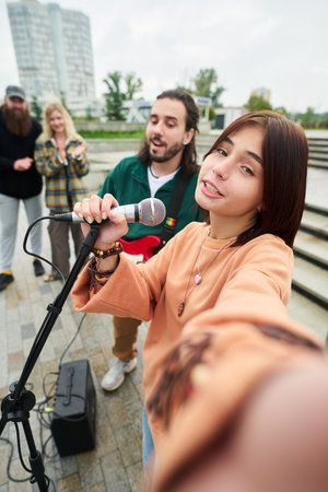 Portrait of Caucasian teenage girl holding microphone and singing into camera while young Caucasian...