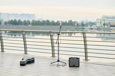 Empty riverside promenade featuring microphone on stand, guitar amplifier, and closed guitar case...