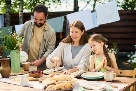 Caucasian middle aged man pouring tea while Caucasian middle aged woman serving pie and Caucasian...
