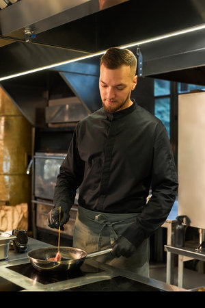 Young adult Caucasian man cooking food in professional kitchen, holding utensil and preparing meal...