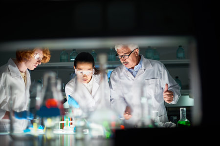 Ambitious scientists bending over table with laboratory glassware. Young woman holding pipette with...