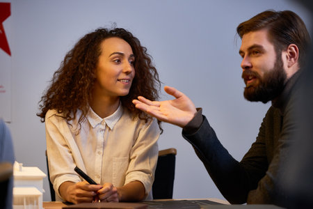 Young successful architects working on house project. Bearded man pointing at something and suggesting new idea while his curly female colleague looking at him with admiration and smilingの写真素材