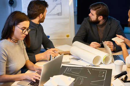 Professional architects having meeting at office, looking at new building draft attached to white...