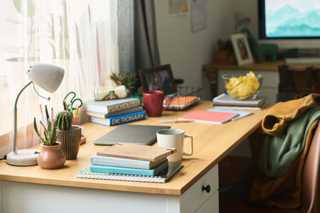 Closeup of organized wooden desk with stack of notebooks, psychology and dictionary books, potted...
