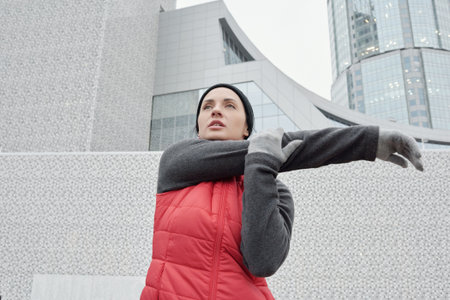 Low angle view of beautiful athletic Caucasian woman in warm sportswear doing physical exercises on...