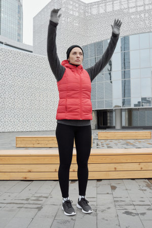 Young attractive Caucasian sportswoman doing warming up exercises before running while standing on background of modern business center outdoorsの写真素材
