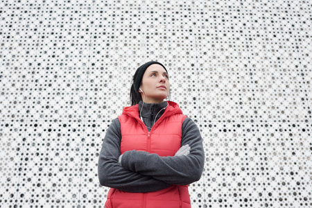 Young attractive female athlete standing outdoors against white perforated wall with crossed hands...