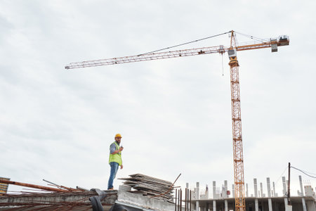 Caucasian middle aged man wearing safety helmet and vest standing on construction site, holding...