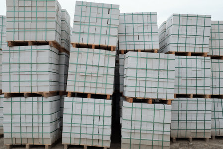 Stacked pallets of building materials arranged outdoors, showing multiple layers of materials...
