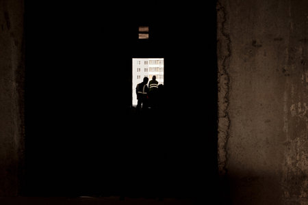 Silhouettes of two men standing in unfinished building corridor, appearing to discuss construction progress, bright window revealing cityscape in backgroundの写真素材