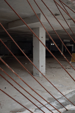 Empty unfinished concrete building showing exposed rusty steel reinforcement bars crossing...