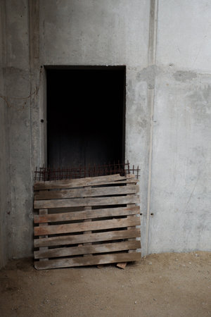 Empty concrete wall featuring open rectangular doorway blocked by wooden pallet and metal rebar,...