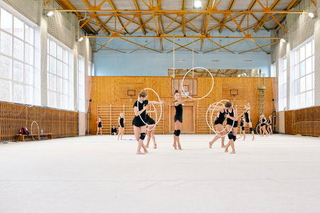 Group of Caucasian girls performing rhythmic gymnastics routine with hoops in sports hall, each child executing coordinated movements, wearing matching athletic outfits, focused on routineの写真素材