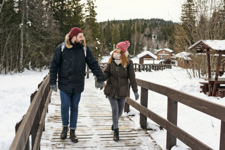 Amorous couple in outwear backpacking together and walking on wooden pathway in snowy natureの写真素材