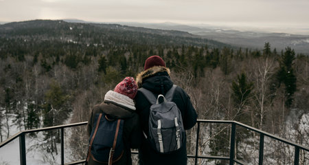 Back view of man and woman with backpacks standing close on viewpoint against highlandsの写真素材