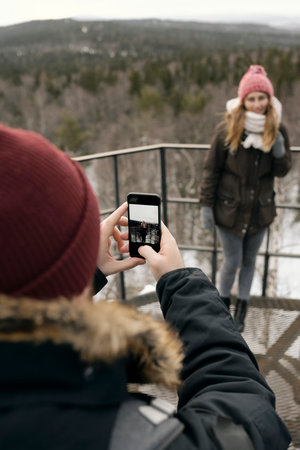 Crop man using phone and taking picture of woman on viewpoint while trekking in highlands togetherの写真素材