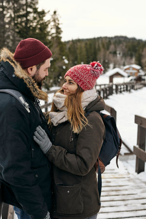 Side view of loving woman and man in outwear standing close while having hiking trip in winter timeの写真素材