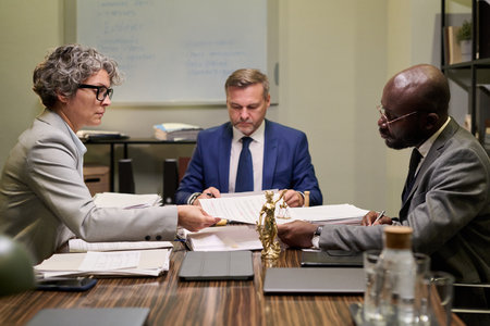 Middle aged Caucasian woman handing document to young Black man, while middle aged Caucasian man...