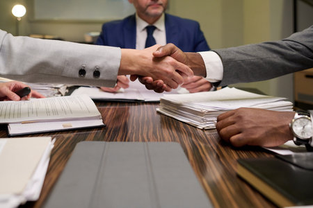 Caucasian woman and Black man shaking hands over stack of documents during business meeting, middle...