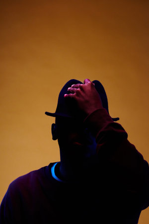 Portrait of young stylish African American male holding hand on his hat while posing in dark studioの写真素材