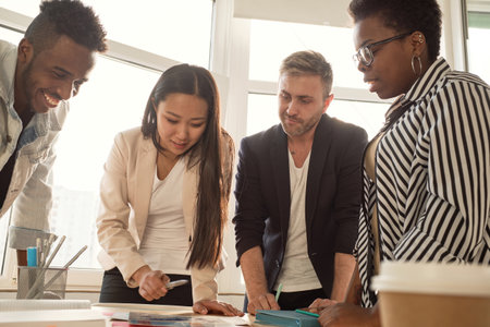 Multiethnic team of young managers working on new project in conference room, standing around table and brainstorming, low angle viewの写真素材