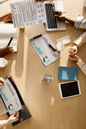 Businessmen having conference in office. Top view of unrecognizable people sitting at large wooden table with gadgets, papers and coffeeの写真素材