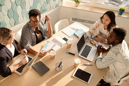 High angle view of young creative office workers of different nationalities sitting at table in...