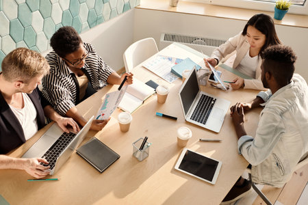 Multiethnic group of young managers sitting around table in conference room and discussing new company strategies, high angle viewの写真素材