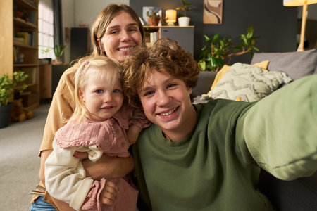 Portrait of Caucasian woman holding Caucasian toddler girl while Caucasian teenage boy taking selfie...
