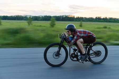Side view portrait of young hipster man rushing fast on retro bike riding in countryside at duskの写真素材