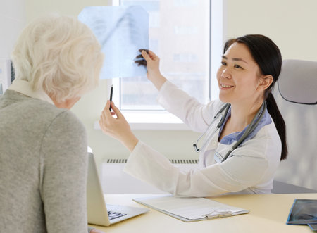 Female physician discussing positive results of MRI examination with female senior patient, showing her radiograph and smilingの写真素材