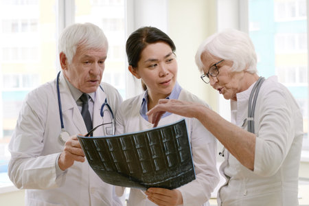 Group of experienced male and female doctors examining X-ray of patient after MRI test in hospital, analysing results and discussing treatmentの写真素材