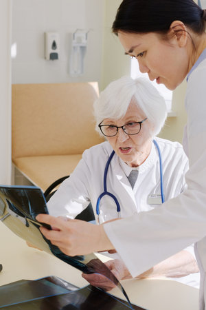 Mature female physician analyzing conditions of patient by looking at his X-ray after MRI scan and...