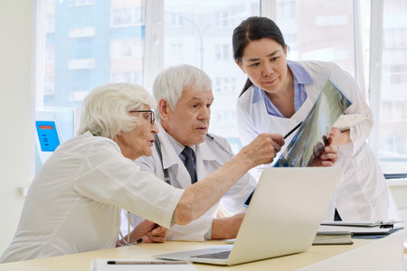 Group of professional physicians consulting together while examining radiographs of patient after...