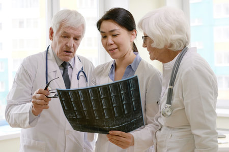 Group of professional male and female physicians looking at radiograph of patient after MRI scan,...