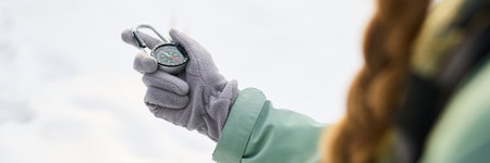 Caucasian young adult woman holding compass in gloved hand while navigating outdoors, partial view showing focus on hand and navigation device against snowy backgroundの写真素材