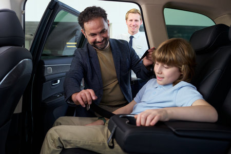Middle aged Caucasian man handing car keys to Caucasian boy sitting in back seat while young Caucasian male car dealerの写真素材