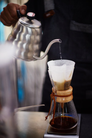 Bali, Indonesia, November 18, 2015. Close up shot of man pouring hot water from gooseneck kettle into paper filter with ground coffee in glass coffee maker, preparing fresh pour over coffeeのeditorial素材