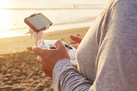 Close up of unrecognizable person operating drone remote controller with mounted smartphone on sandy...