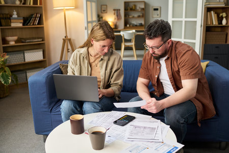 Caucasian young adult woman using laptop while Caucasian young adult man reviewing financial...
