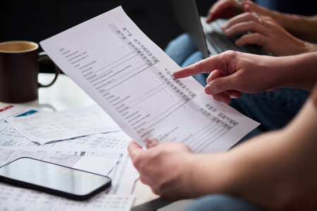 Caucasian middle aged man reviewing tax documents and using laptop while sitting at desk, holding...