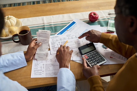 Middle aged Black man and middle aged Black woman reviewing tax documents together at table, using calculator and receipts, discussing financial paperwork related to paying taxesの写真素材