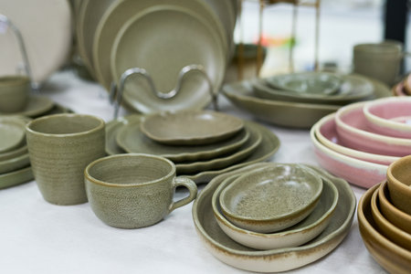 Ceramic tableware set featuring plates, bowls, cups, and saucers arranged on surface, showcasing variety of shapes and sizes with neutral and pastel tones, no people visibleの写真素材